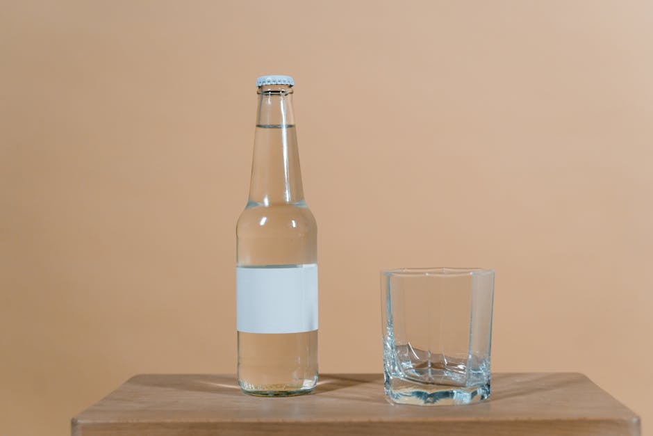 Clear glass bottle and cup on wooden surface with a soft brown background.